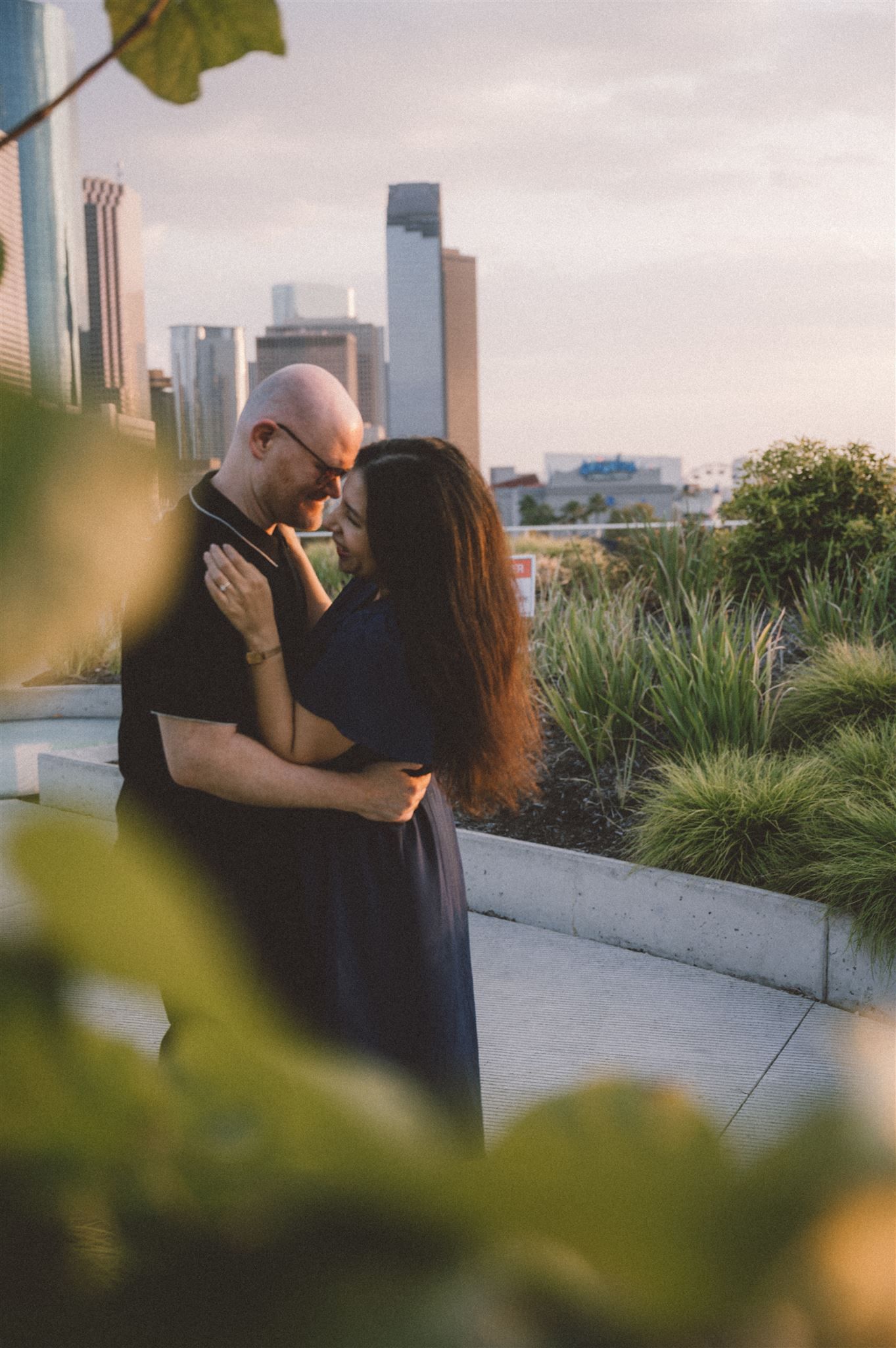 A romantic couple embraces with Houston's downtown skyline visible through foliage.