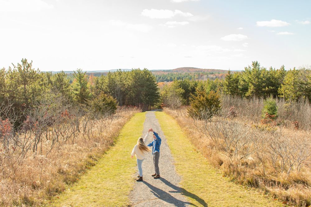 A couple walking hand in hand down a scenic trail surrounded by autumn foliage.