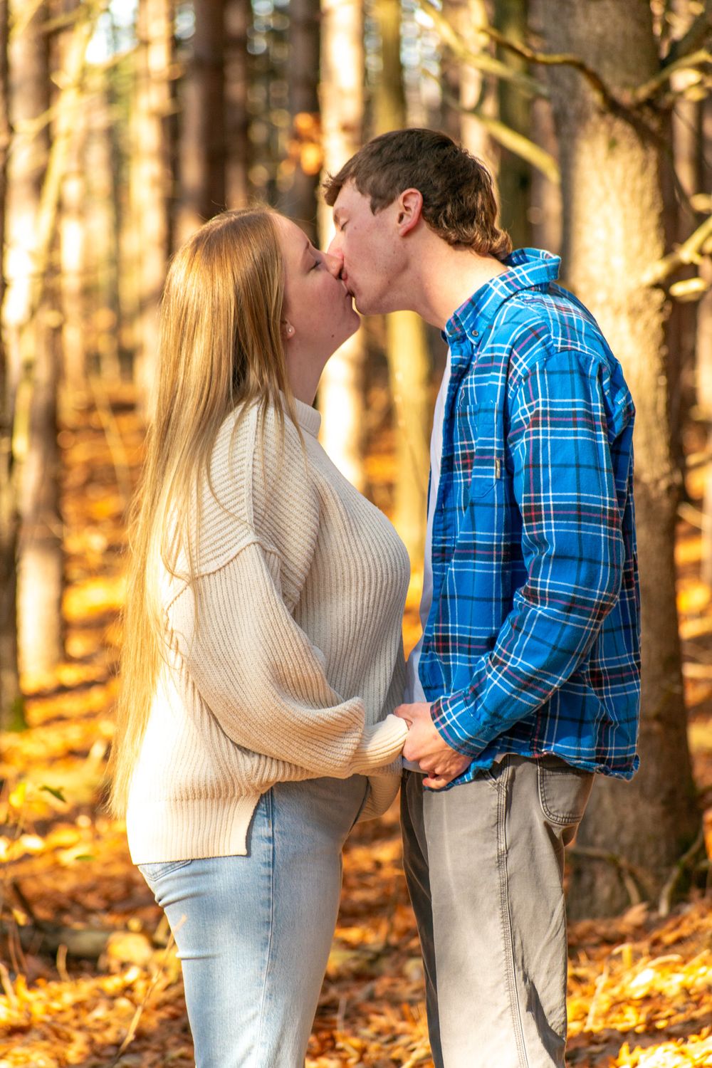 A romantic autumn scene with a couple sharing an intimate moment in a sunlit forest.