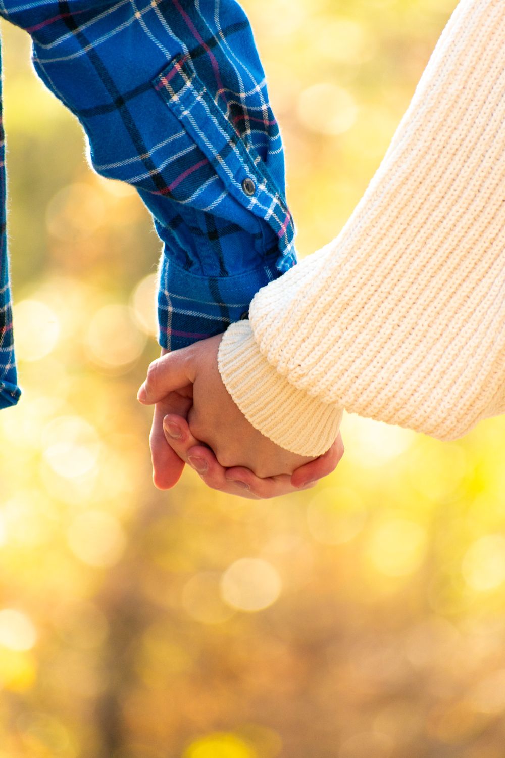 Close-up of intertwined hands with contrasting blue plaid and cream sweater sleeves.