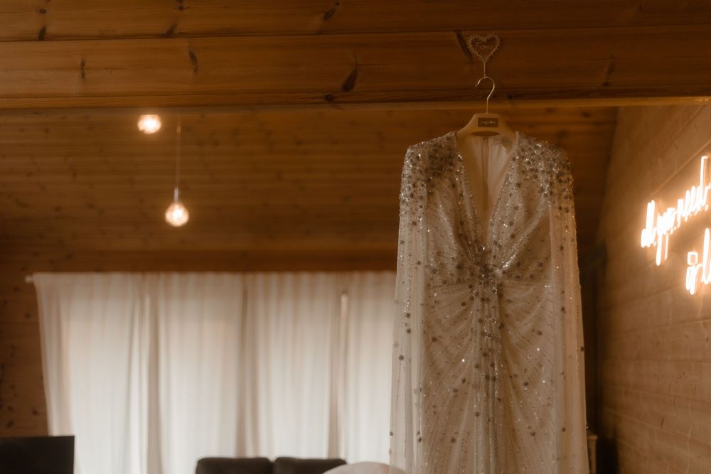 A sparkly beaded wedding dress hangs elegantly against a white backdrop with warm lighting.