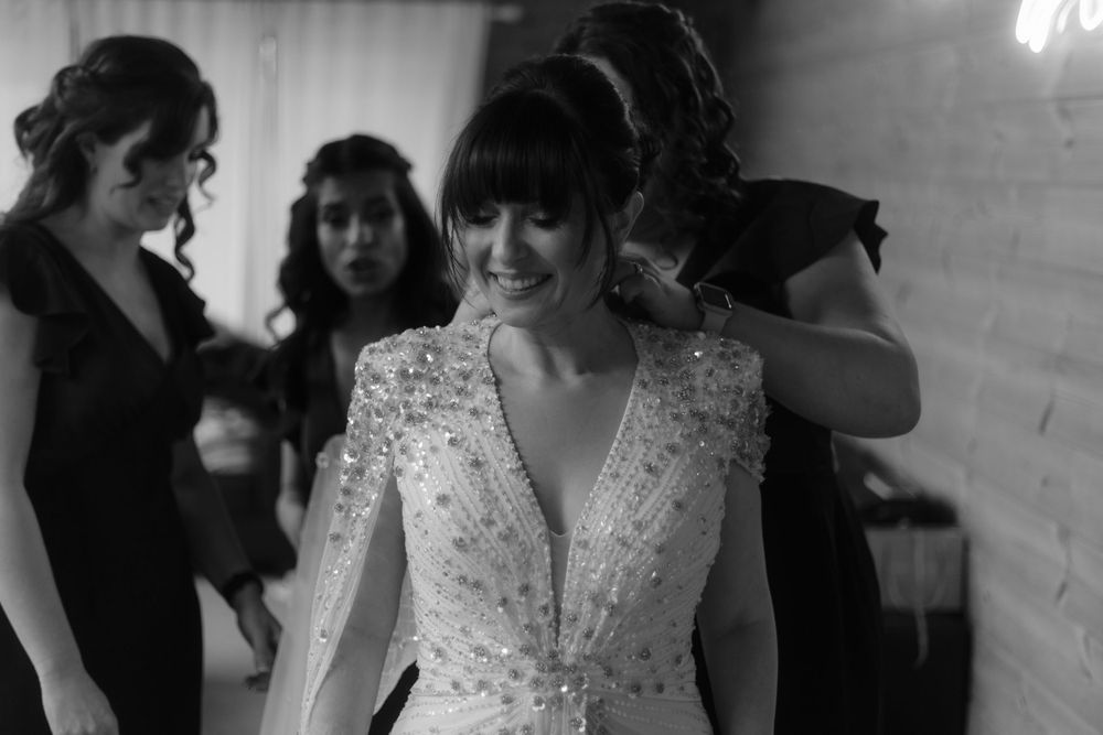 Bride wearing a beaded white wedding gown getting ready with bridesmaids in black dresses.