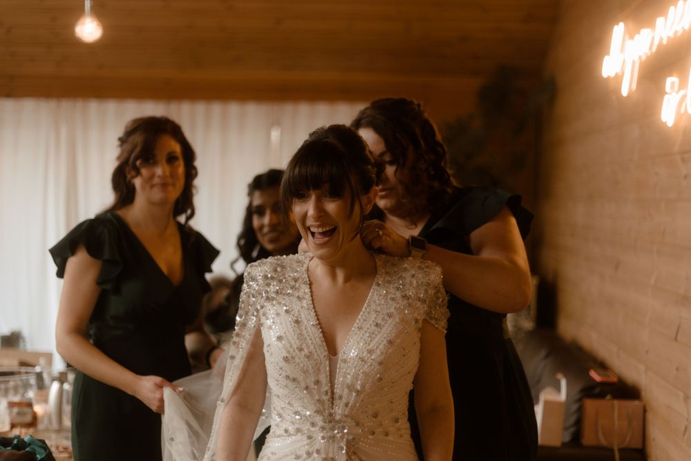 A bride in a sparkly V-neck wedding dress smiles while getting ready with her bridal party.