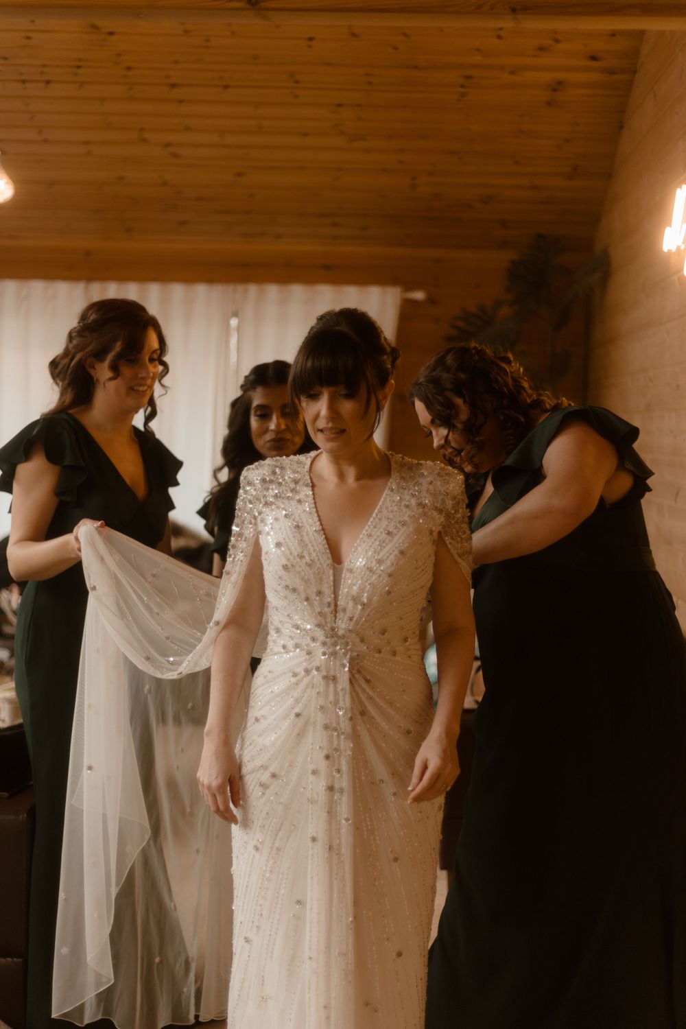 Wedding preparations showing bridesmaids in black dresses helping adjust the bride's beaded gown.
