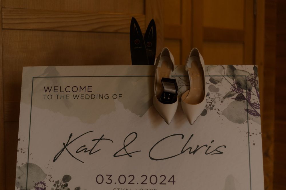 Wedding welcome sign for Kat & Chris with bridal shoes arranged above.