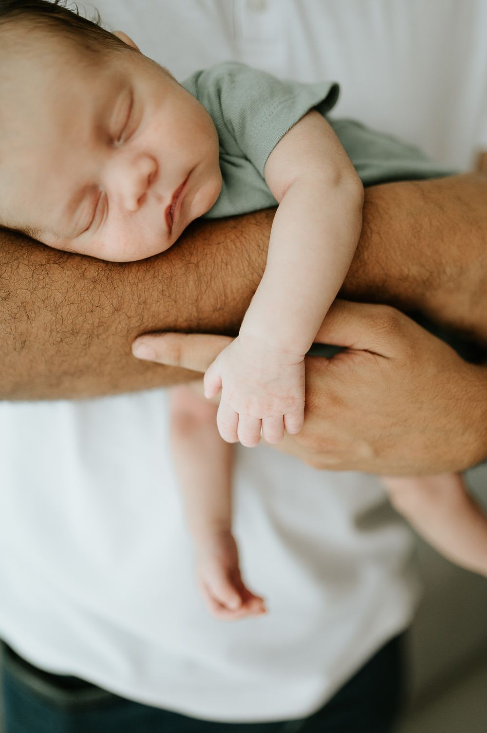 Sleeping baby in mint green onesie resting peacefully on arm.