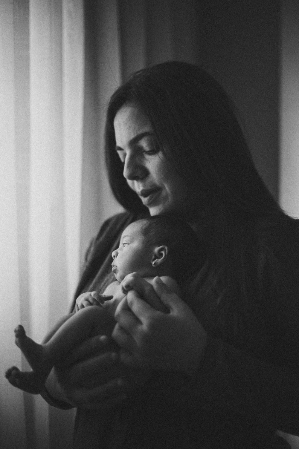 Atmospheric black and white photograph of quiet parenting moment by window.