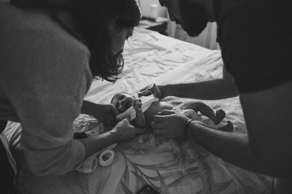 Parents tending to newborn on bed in moody black and white photograph.
