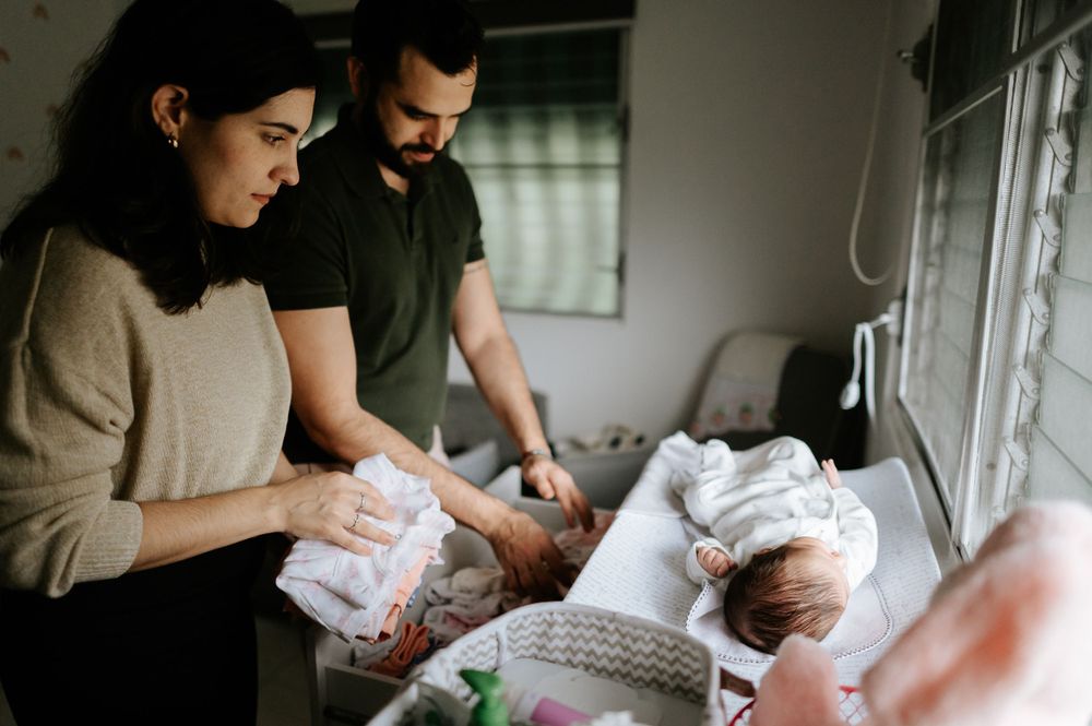 Parents attending to their newborn by a sunlit window in a cozy nursery.