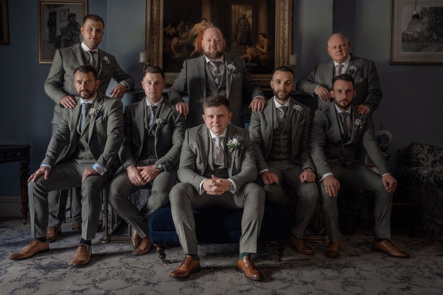 Group portrait of groomsmen in matching gray suits seated in an elegant room.