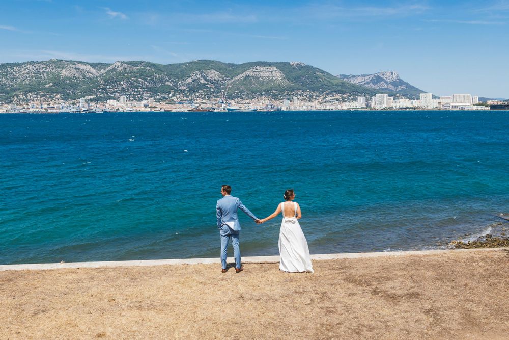 Couple standing on Mediterranean beach with mountain vista and turquoise waters.
