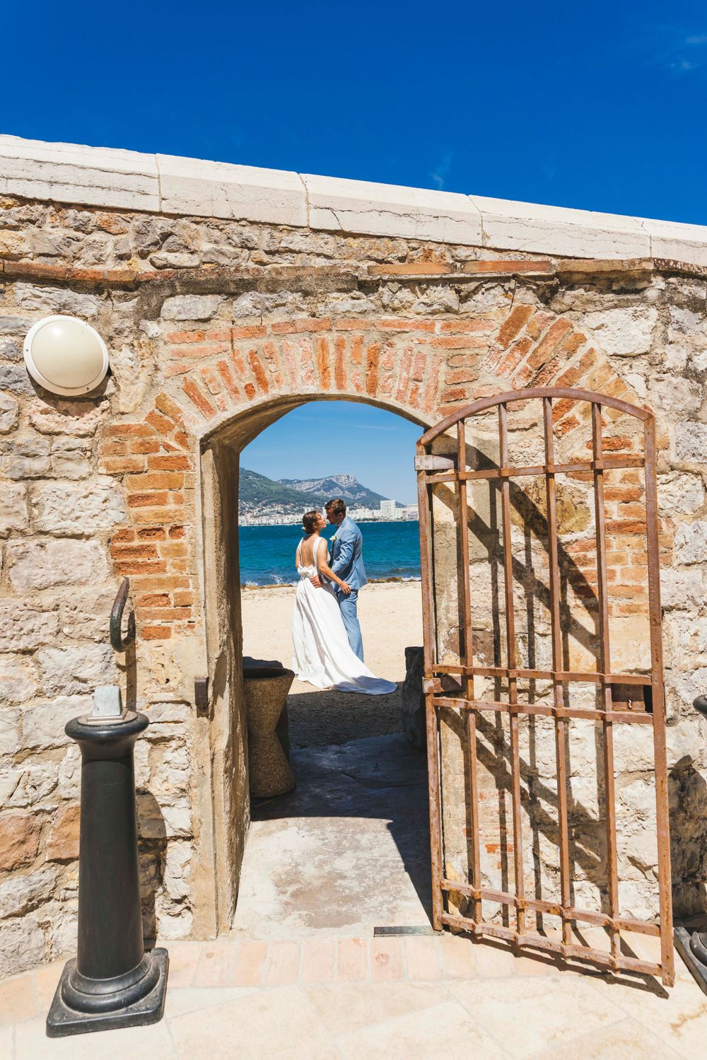 Stone archway framing a coastal view with turquoise waters and mountains in the background.