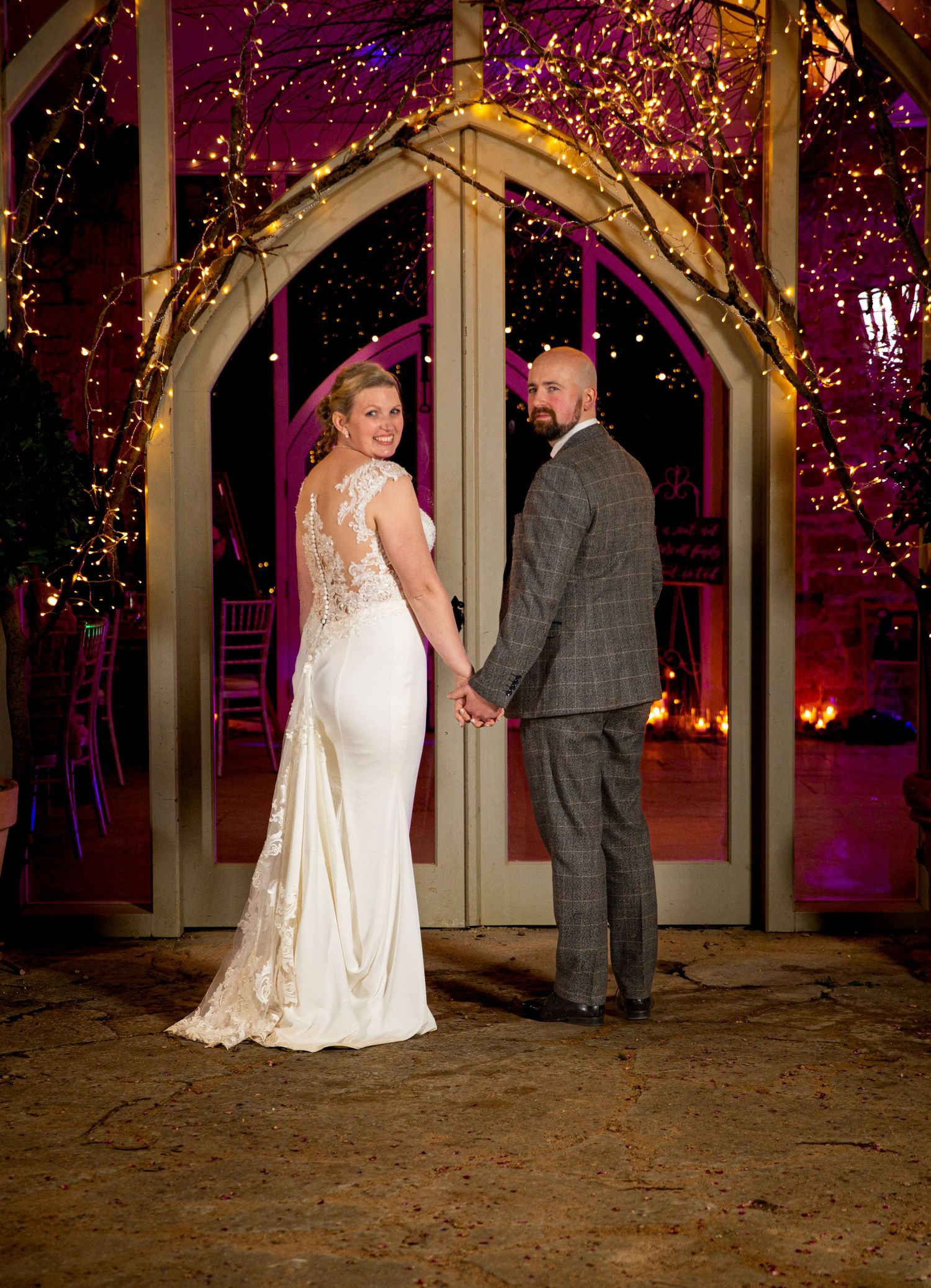 Couple poses under romantic purple lighting in an elegant venue with glowing decorations.