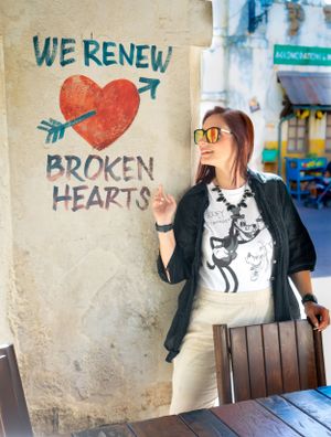 Person in casual attire poses near wall with 'We Renew Broken Hearts' graffiti art.