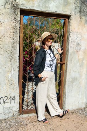 Figure in overalls and hat posing against weathered wall with rustic windows.