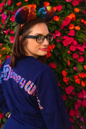 Close up view of a navy sweatshirt with colorful sequined text against a background of vibrant red flowers.