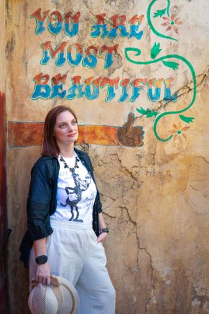 Someone in white overalls and denim jacket stands by colorful graffiti wall with turquoise text.