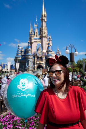 Teal Disney World balloon and Cinderella Castle backdrop with colorful flowers in foreground.
