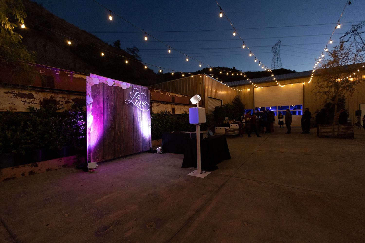 String lights illuminate an outdoor venue at night with purple uplighting and decorative elements creating an ambient atmosphere.