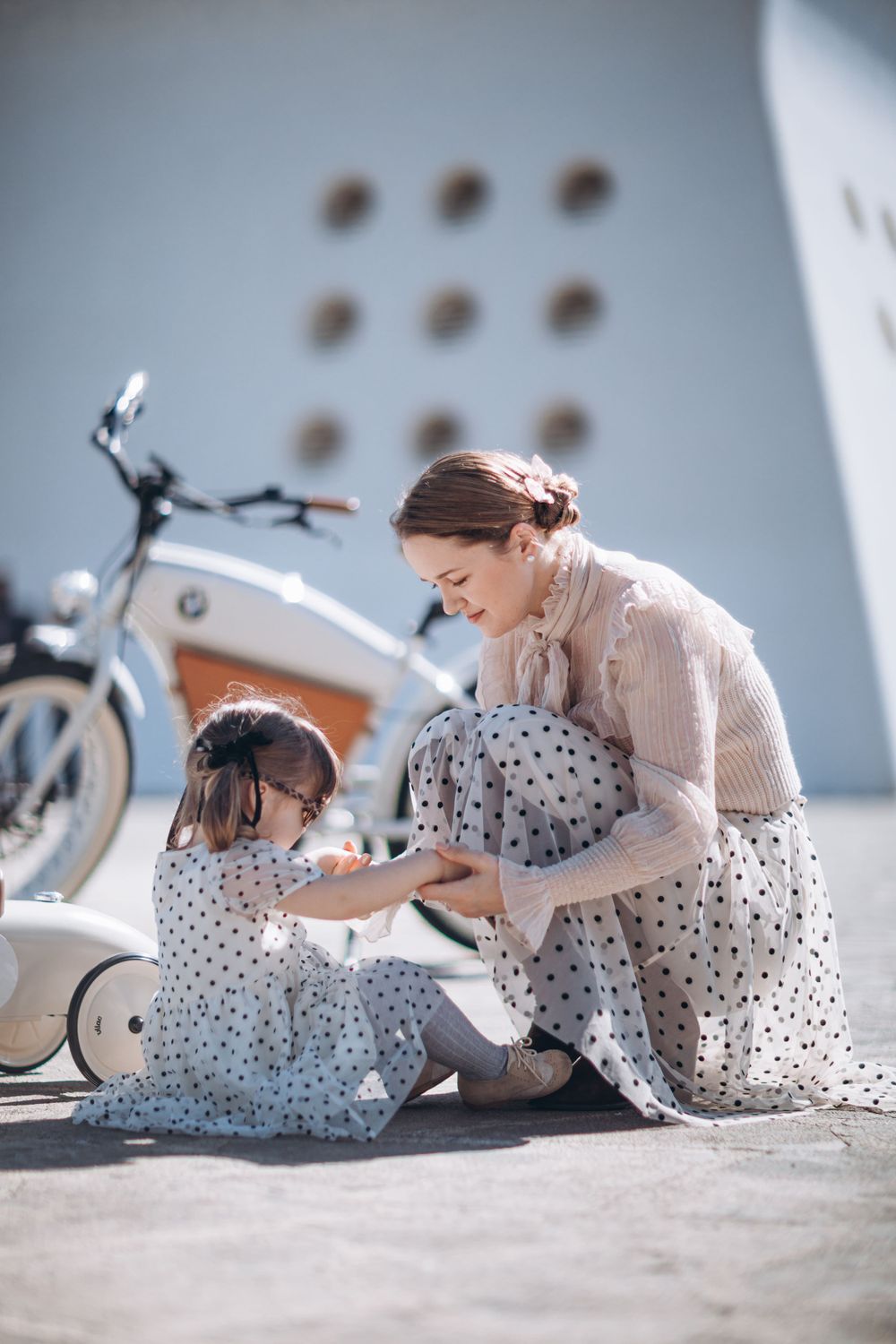 Two people in polka dot dresses sharing a tender moment near vintage scooters.
