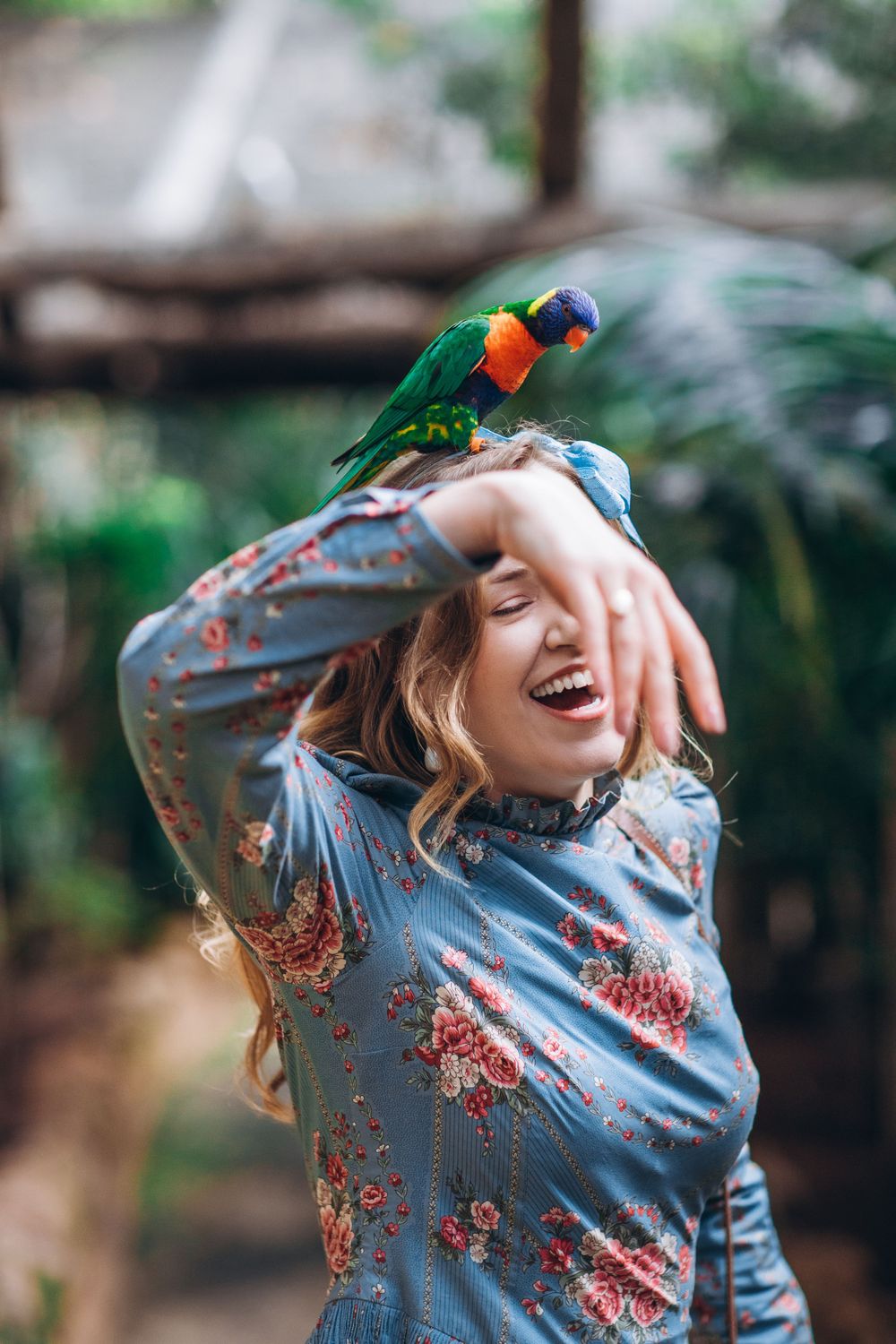 Person in floral dress laughing joyfully with sunlight filtering through trees.