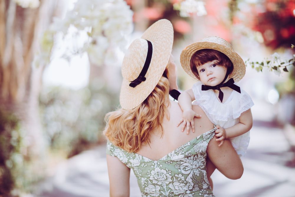 Two people in matching straw hats pose together under flowering spring blossoms.