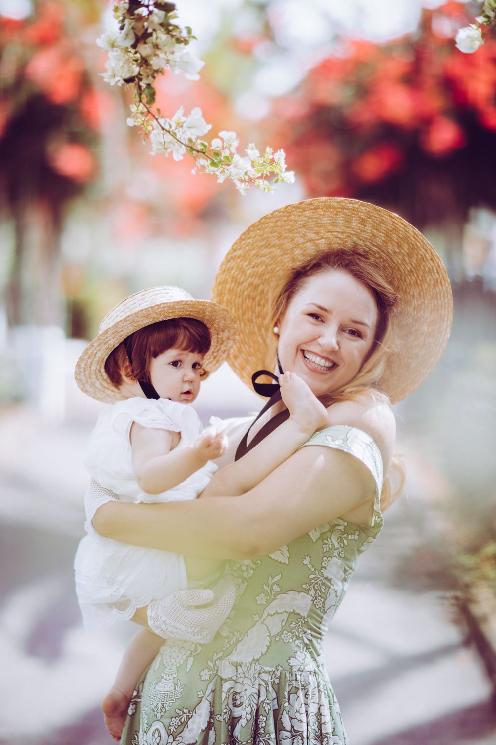 A sweet outdoor portrait under cherry blossoms featuring matching straw hats and floral outfits.