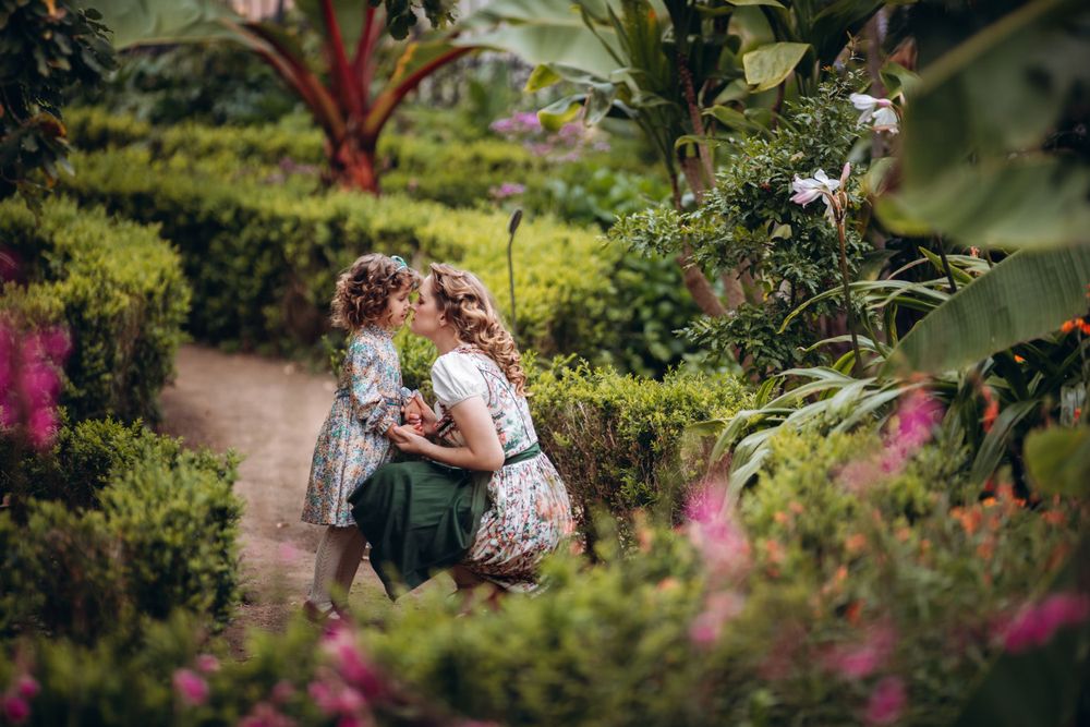 Two figures embrace among colorful flowers in a lush garden setting.