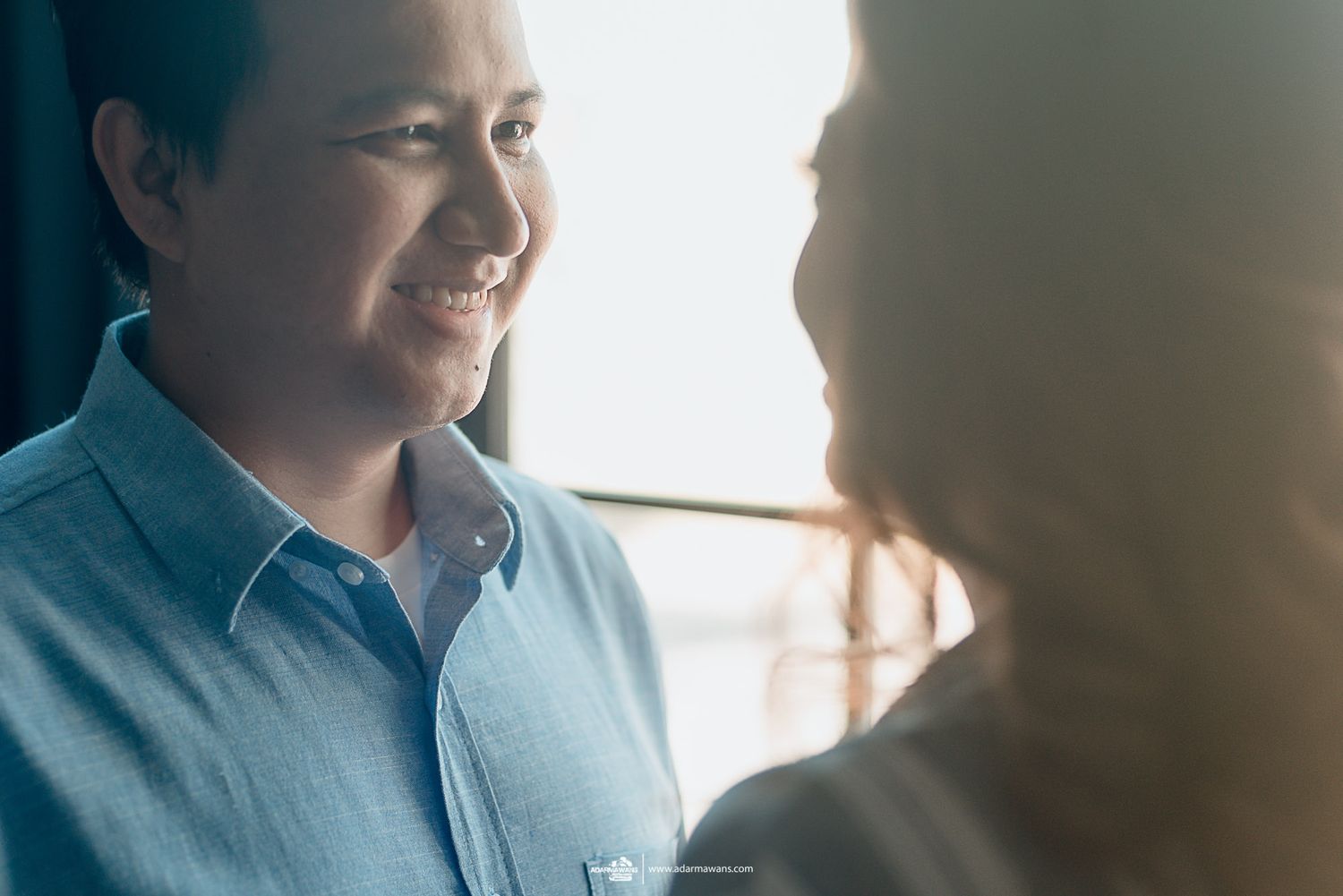 A candid moment shows a couple sharing a joyful interaction in natural window light.