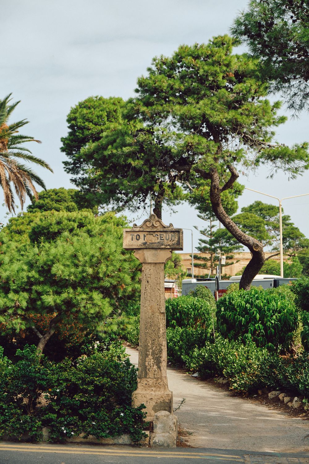 Stone pillar marker surrounded by lush greenery and palm trees in a Mediterranean garden.