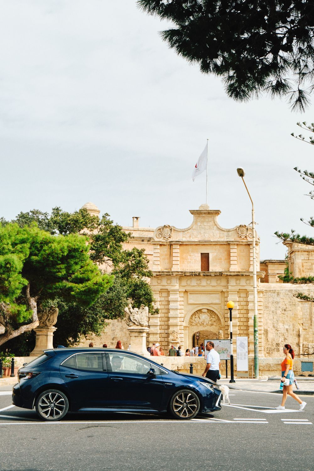 Historic limestone city gate entrance with black car and trees in foreground.
