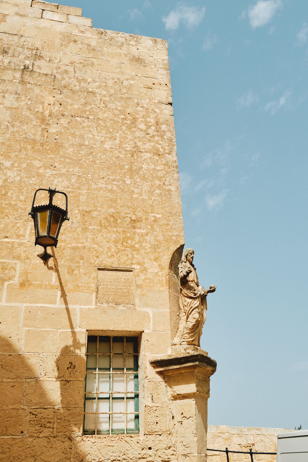 Medieval limestone wall with decorative statue and lantern fixture in Malta.