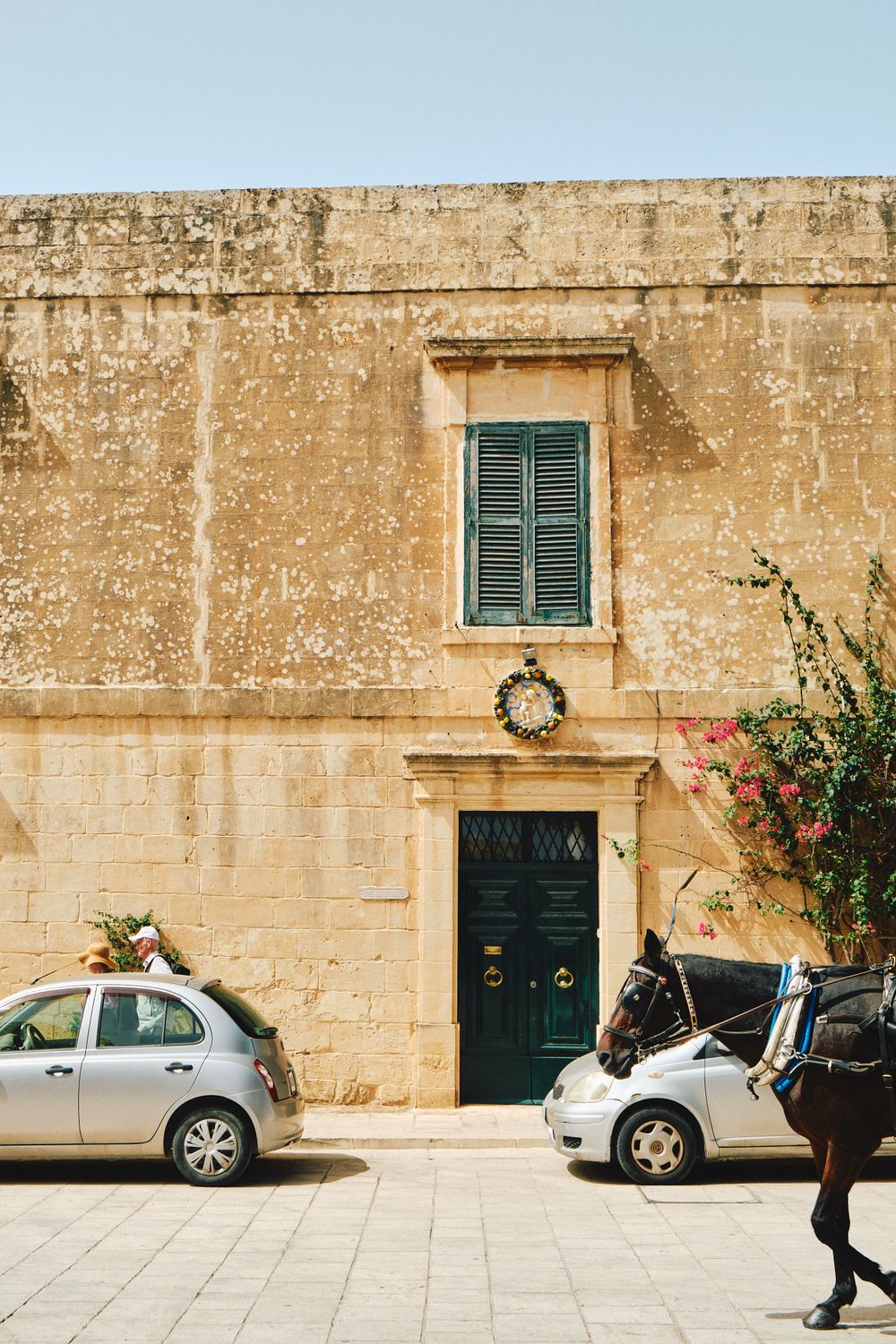 Traditional Maltese building facade with green shuttered window and parked cars.