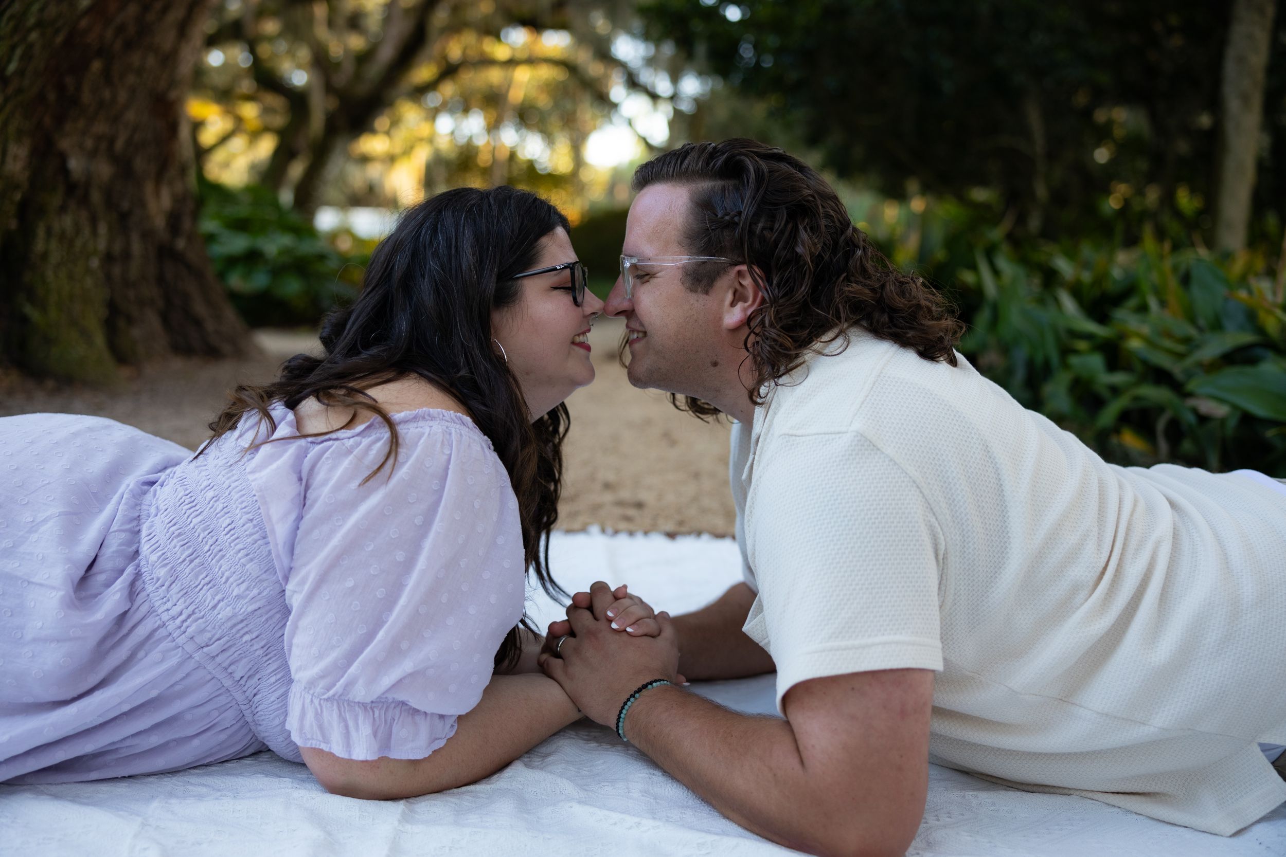 Couple sharing intimate moment while laying on white blanket outdoors.