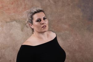 Expressive portrait with blonde updo hairstyle against textured brown studio background.