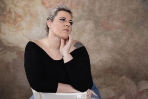 Thoughtful studio portrait with hand on chin against mottled brown background.