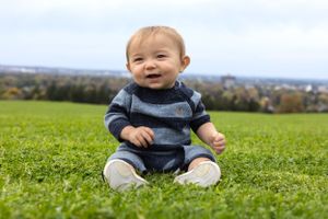Young child wearing a striped sweater sitting on grass with a scenic view.