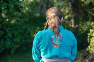 Back view of turquoise martial arts uniform showing detailed dragon embroidery design.