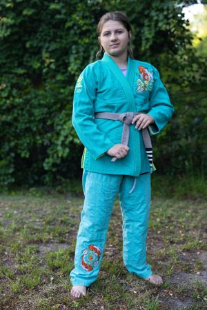 Person wearing bright turquoise martial arts uniform with decorative floral embroidery stands outdoors.