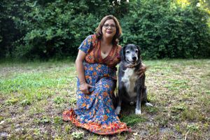 A person in a floral dress sits on grass with their friendly black and white dog in a garden setting.