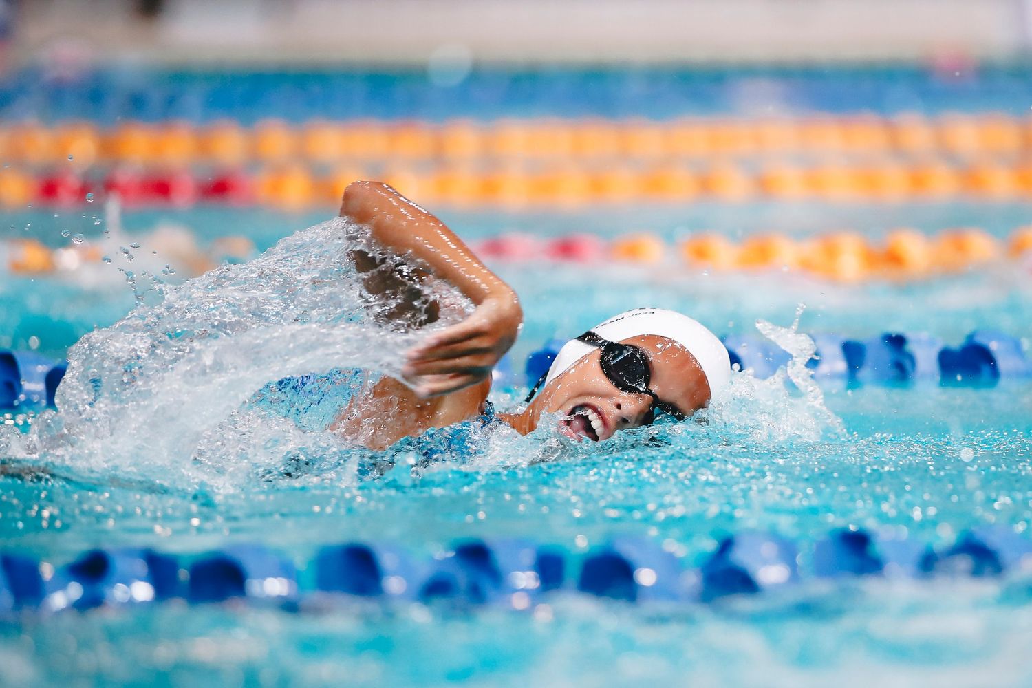 Swimmer performing freestyle stroke in competitive pool with blue lane dividers.