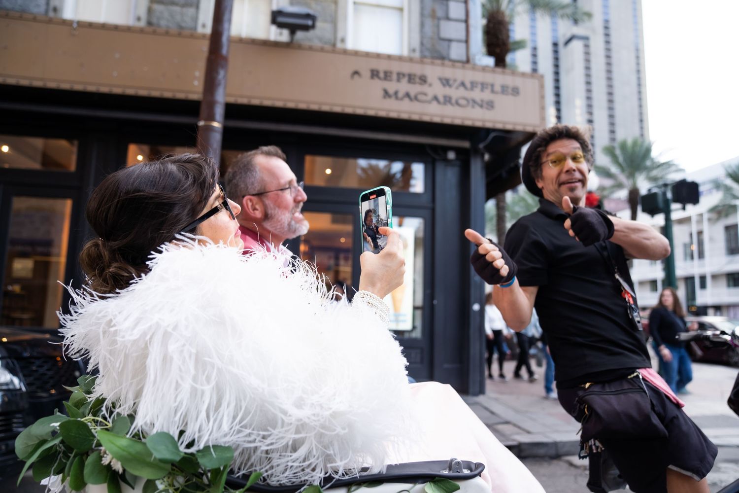 Celebratory scene outside urban storefront with feathered white dress.