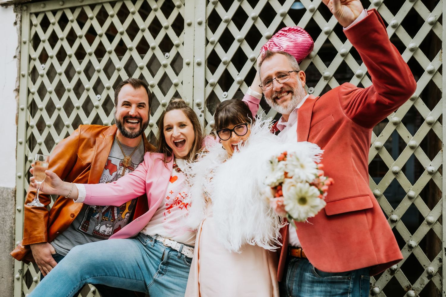 Group celebrating joyfully in front of white lattice backdrop with confetti and flowers.