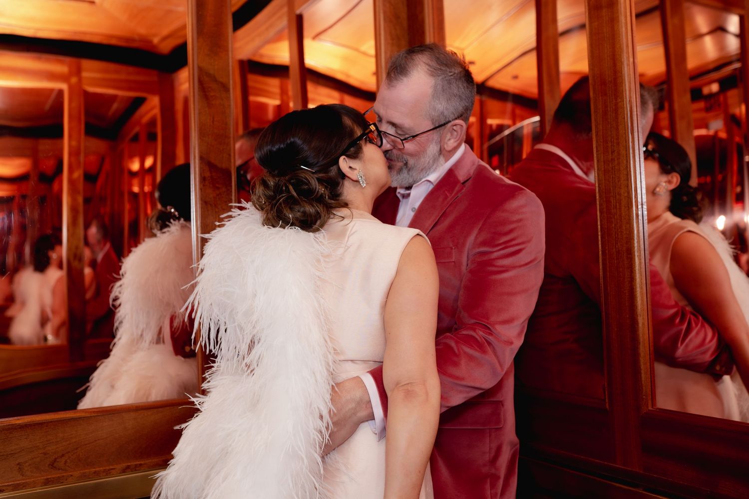 Romantic moment between couple in formal wear with feathers against warm wooden interior.