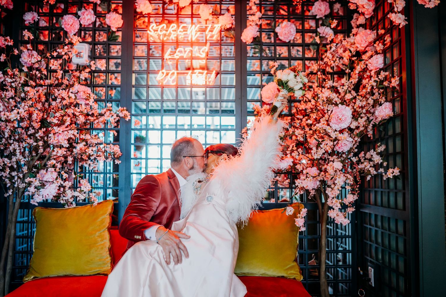 Wedding scene with pink cherry blossoms and yellow cushions against lattice backdrop.