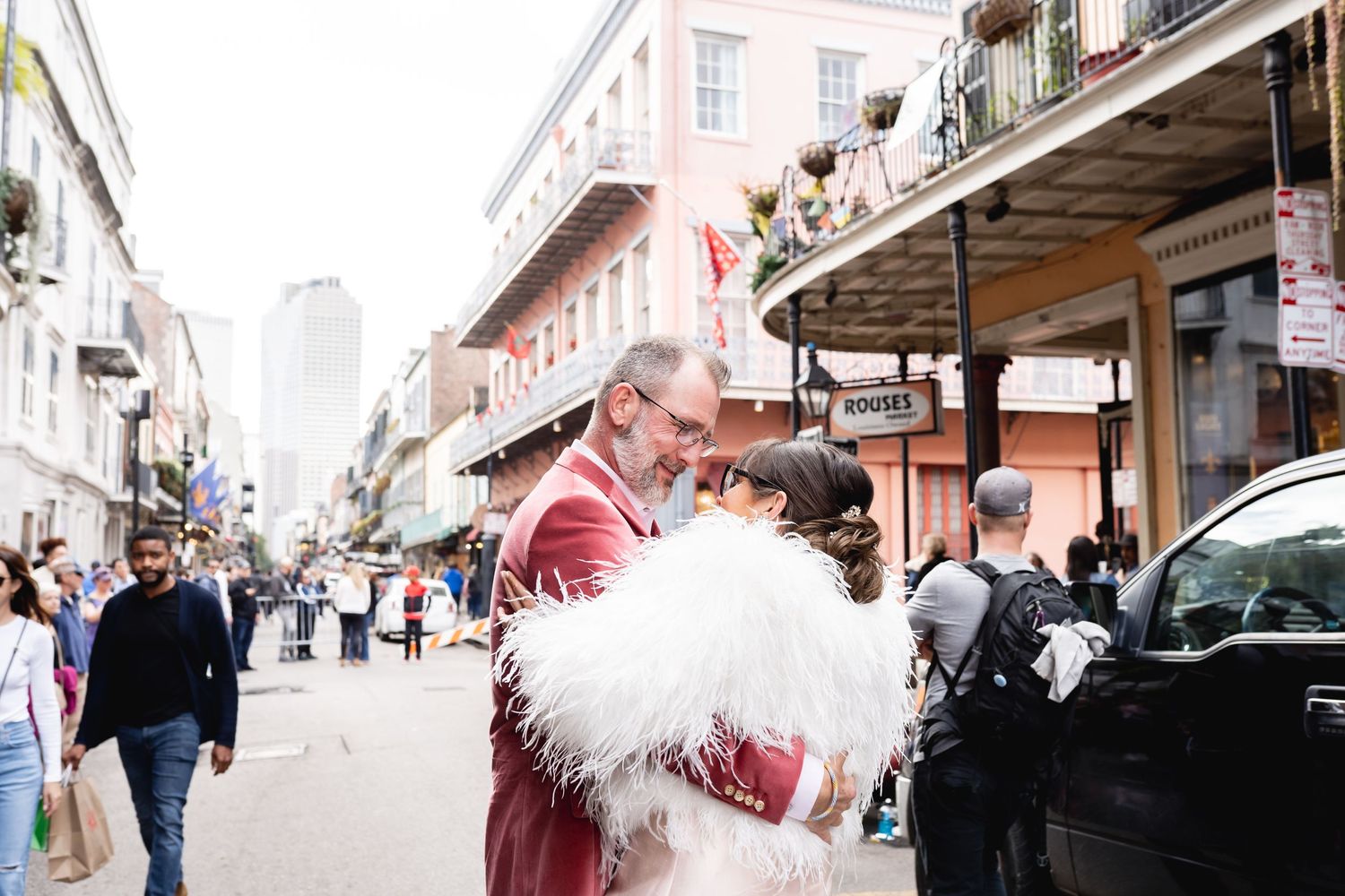 A couple embraces on a lively New Orleans street with historic buildings in the background.