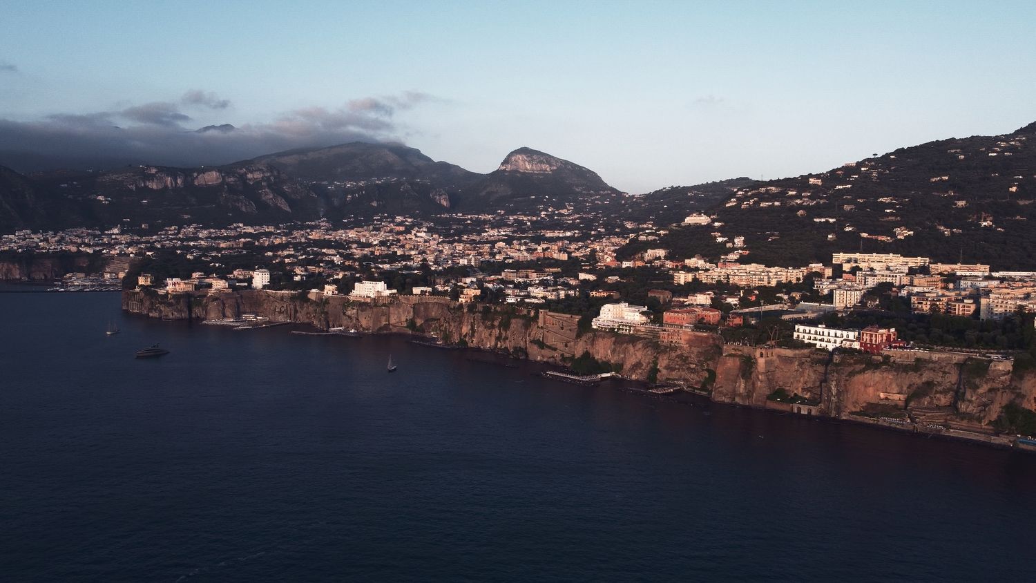 Aerial view of coastal Mediterranean town nestled between mountains and sea at dusk.