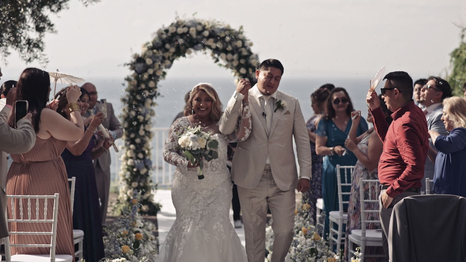 Wedding ceremony under floral arch with guests celebrating newlyweds' exit.
