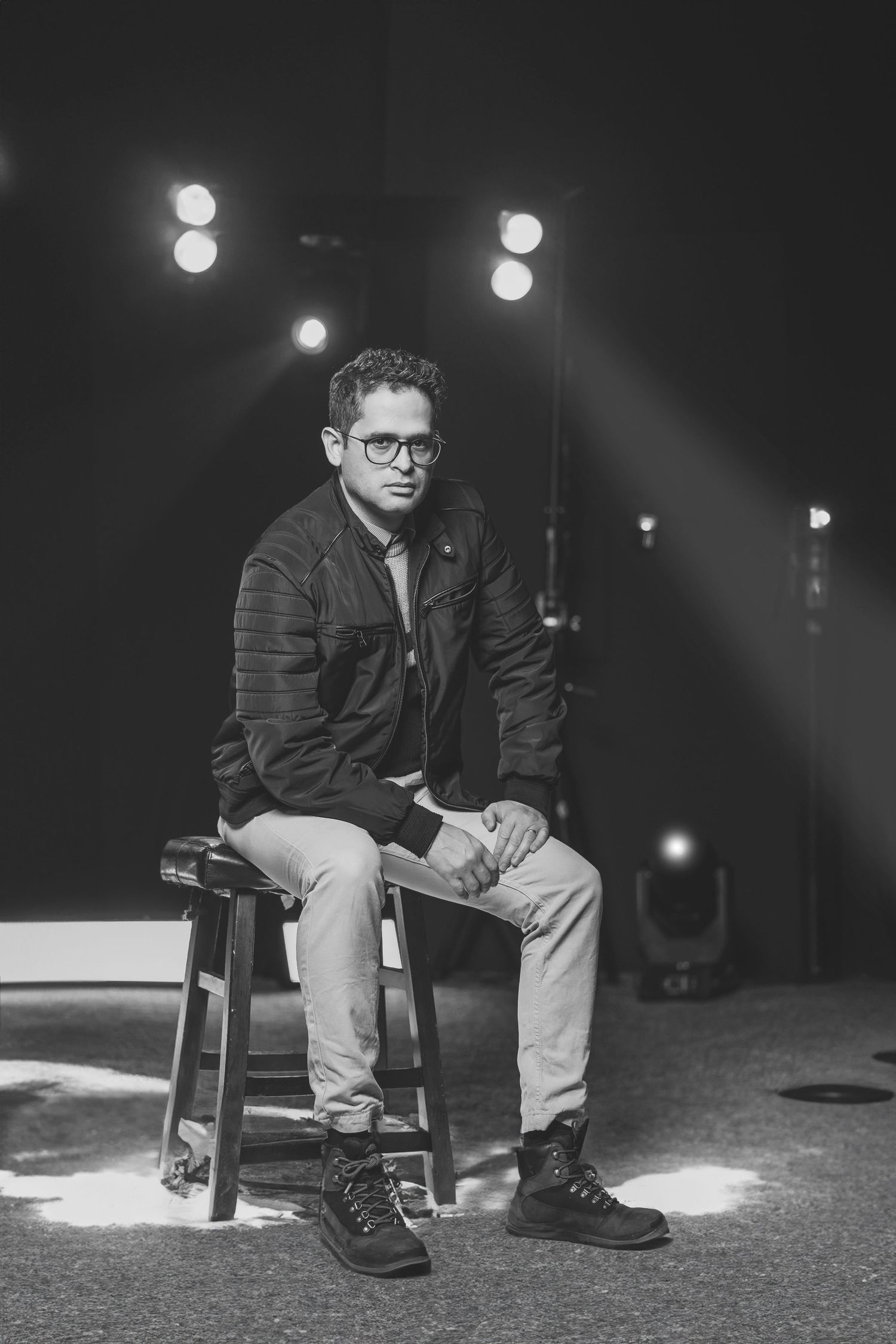 Black and white photos of person sitting on chair in dark stage setting with dramatic spotlight lighting.
