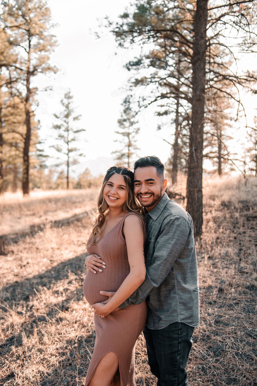 Romantic maternity photo session in a wooded area with golden sunlight.